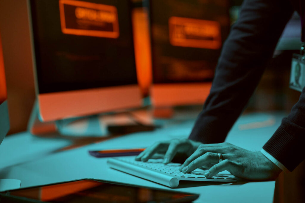Hands typing on a computer keyboard with code displayed on a screen
