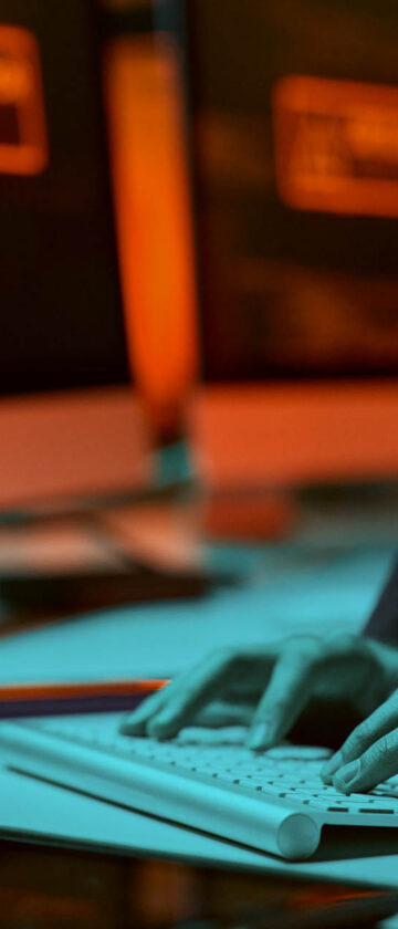 Hands typing on a computer keyboard with code displayed on a screen