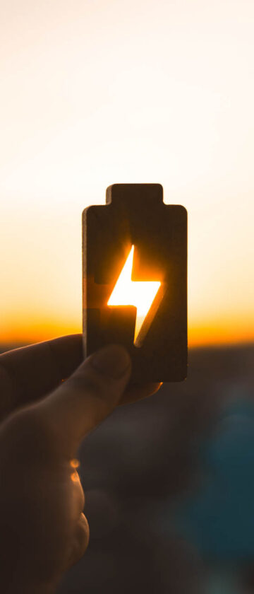 A battery with an energy symbol against a sunset